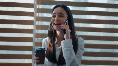 Neşeli gülen Kafkasyalı iş kadını cep telefonundan konuşuyor Avrupalı iş kadını konuşuyor akıllı telefon çağrısı yapıyor çay içiyor gülüyor mutlu iletişim kuran kadın ofiste neşeli haberler tartışıyor