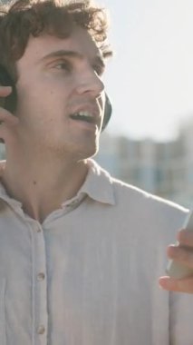 Kablosuz kulaklıklarla gülümseyen Kafkasyalı iş adamı cep telefonu dinleyen iş adamı adam, cep telefonu cihaz işadamı. Şarkıyı iyi dinle. Ses kalitesi kulaklıklar güneşli şehirde dinlenmenin keyfini çıkarıyor.