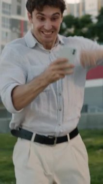 Neşeli Kafkasyalı iş adamı cep telefonu cihazını kazanmasına hayret etti. Akıllı telefon zaferi olan profesyonel bir erkek iş adamı. Şehirdeki internet üzerinden kurumsal finansal fırsatı kazandı.