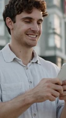 Mutlu gülümseyen Kafkasyalı iş adamı elinde cep telefonu, neşeli iş adamı gülüşüne bakıyor. İyi haber mesajının tadını çıkar. İnternet sitesinde gezen erkek geliştirici şehir merkezinde cep telefonu kullanıyor.