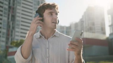 Kablosuz kulaklıklarla gülümseyen Kafkasyalı iş adamı cep telefonu dinleyen iş adamı adam, cep telefonu cihaz işadamı. Şarkıyı iyi dinle. Ses kalitesi kulaklıklar güneşli şehirde dinlenmenin keyfini çıkarıyor.