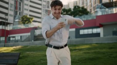 Neşeli Kafkasyalı iş adamı cep telefonu cihazını kazanmasına hayret etti. Akıllı telefon zaferi olan profesyonel bir erkek iş adamı. Şehirdeki internet üzerinden kurumsal finansal fırsatı kazandı.