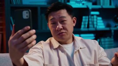 Neşeli Asyalı adam, cep telefonuyla video görüşmelerini selamlıyor. Mutlu Koreli orta yaşlı, gülümseyen Çinli Çinli kullanıcıya merhaba deyin.