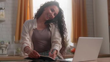 Mutlu Latin iş kadını cep telefonuyla konuşan, dizüstü bilgisayar yazan, notlar yazan, bilgisayar akıllı telefon kullanan, gülümseyen, İspanyol bayan iş kadını, ev sahibi, uzaktan kumandalı ev sahibi.