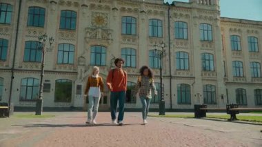 Kampüste zıplayan üç çok ırklı öğrenci kampüs üniversitesini kutluyor mutlu arkadaşlar Afrikalı adam erkek beyaz kadın kız liseler açık hava tatilleri sınavlarını bitirdiler.