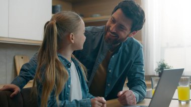 İnternet teknolojisiyle mutlu beyaz bir aile mutlu bir ebeveyn, mutlu bir çocuk, evde uzaktan gülümsemeyi öğreniyor. Mutfaktaki baba, bilgisayardaki bilgisayar oyununa yardım etmeyi seviyor.