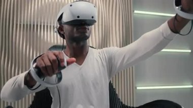 Beyaz fütürizm stüdyosundaki Afrikalı Amerikalı siber adam VR gözlük takan fütürist erkek sanal gerçeklik miğferi 3D alan yenilikçi modern teknolojiyi iş oyunları eğitimi için kullanıyor.