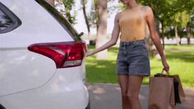 Neşeli Afro-Amerikalı kadın alışveriş çantalarını şehrin dışındaki araba bagajına koyuyor mutlu kadın alıcı iş kadını paketleri yüklüyor tüketici otomobil satın alıyor şehir dışında şehir dışında araba satın alıyor
