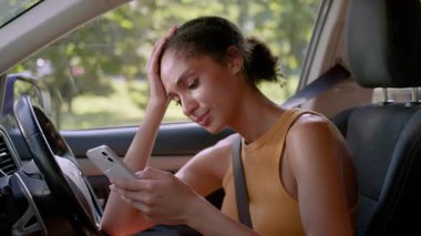 Baş ağrısı çeken Afrika kökenli Amerikalı bir kadın cep telefonlu akıllı telefon sohbetine çevrimiçi olarak cevap veriyor. Kadın iş kadını araba otomobili araç şoförü araç taşıma aracı mesaj aracı.
