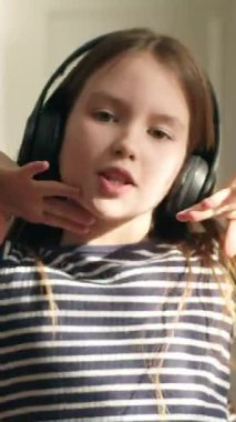 Kafkasyalı mutlu küçük kız çocuk kulaklıklar takıyor müzik dinliyor kameraya bakıyor gülümsüyor dans ediyor evde tatmin olmuş kız neşe içinde zıplıyor