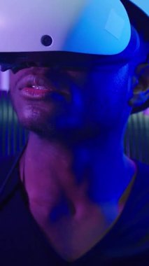 VR miğferli, karanlık neon fütüristik uzay kumandalı, sanal gerçeklik yazılım oyunu, kapalı mekanda oynayan erkek siber-punk oyun yenilikçiliği meta-evren kullanan odaklı Afrikalı Amerikalı adam.