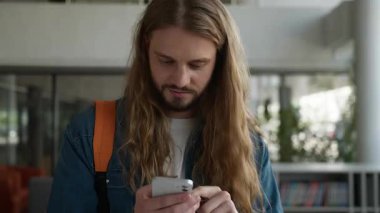 Cep telefonu zaferiyle kazanan Avrupalı beyaz erkek öğrenci üniversite akademisinde kamera heyecanına bakarak mutlu mesut gülen akıllı telefonla iyi haberler alıyor.