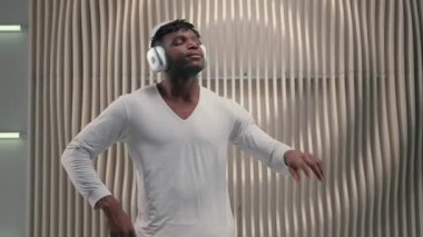Fütürist odada müzik dinleyen, kulaklıklı, kulaklıklı, beyaz fütürizm stüdyosunda çalan, dinamik hareketlerle tek başına dans eden, Afro-Amerikan bir adam.