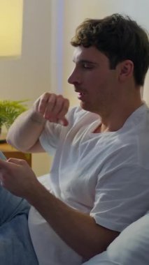 Uykulu yorgun Kafkasyalı adam yatak odasında uzanıyor cep telefonuyla esniyor sosyal medya tembelliği yapıyor Avrupalı sıkılmış erkek adam akıllı telefon sohbetleri yapıyor kapalı mekanda uyanış teknolojisi hakkında konuşuyor.