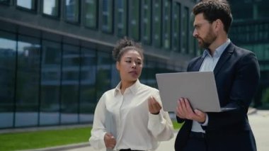 Çok ırklı iş arkadaşları Kafkasyalı erkek Afrikalı kadın şehir yürüyüşü tartışırken iş konuşmaları dizüstü bilgisayarlı takım çalışması anlaşmazlığı görüşmeleri çeşitli iş adamları kadın işadamları sokak dışında