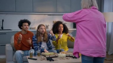 Multiracial friends playing charades guessing game at home room Caucasian woman gesturing explaining word fun entertainment diverse African women and men pantomime joyful group laugh interact together