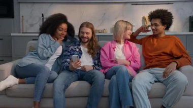 Gülümseyen çok ırklı arkadaşlar cep telefonu uygulaması kullanan kadınlar, sosyal medya videolarını evde izliyorlar, birlikte, Afro-Amerikalı erkekler, beyaz kızlar, kadın erkekler, arkadaşlığın tadını çıkarıyorlar, çok ırklı eğlence.