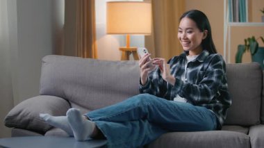 Mutlu Asyalı kadın koltukta oturmuş, akıllı telefondan zaferi kutluyor cep telefonu oyunu oynayan Koreli kadın iyi haberler okuyor, internette iyi şanslar diliyor.