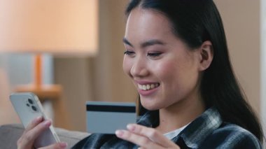 Elinde banka kartı ve cep telefonu tutan Asyalı kadın internet üzerinden ödeme yapıyor. Gülümseyen Koreli Çinli kadın e-ticaret alışverişi biletleri alıyor. İnternet üzerinden alışveriş yapıyor.