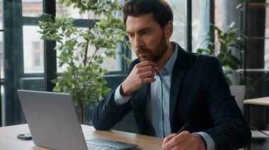 Düşünceli şaşkın Kafkasyalı ofis işadamı bilgi analizi yaparken bilgisayar uzmanı erkek girişimci yönetici kullanarak notlar yazıyor iş adamı adam.