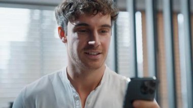 Kafkasyalı neşeli iş adamı cep telefonuyla ofiste akıllı telefon işadamını kullanarak yürüyor sohbet eden alet bağımlısı şirkette çalışıyor sosyal medya telefon uygulaması okuyan erkek adam işçi