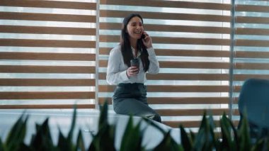 Olumlu gülümseyen Kafkasyalı iş kadını konuşuyor. Telefonda gülüyor. Kahve içiyor, iş kadını içiyor.