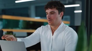 Yorgun, uykulu, esneyen Kafkasyalı iş adamı internette fazla mesai yapıyor, bilgisayarını kapatıyor, yorgun iş adamı esniyor, internet işini bitiriyor, erkek adam enerji sorunu yaşıyor, akşam ofisinde kronik uykusuzluk çekiyor.