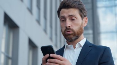 Şehirdeki Kafkasyalı yetişkin işleri üzgün cep telefonlu olgun iş adamlarının akıllı telefondan kötü haberler okuması olumsuz mesajlar tatmin olmamış erkek memnun değil ve internet başvurusu reddediliyor.