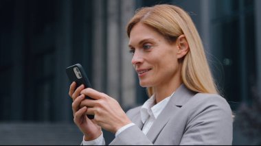 Gadget bağımlısı, neşeli Kafkasyalı 40 'lı yaşlarda iş kadını cep telefonu kullanıyor. Ofiste iş kadını, akıllı telefon yazıcısı, kadın girişimci cep telefonuyla şehir merkezine giriyor.