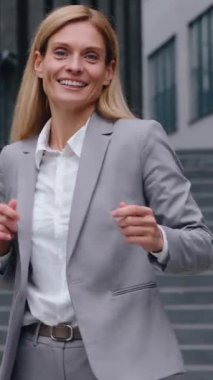 Mutlu Kafkasyalı orta yaşlı iş kadını dans ederek şehirde zıplıyor, gülümsüyor aktif iş kadını kadın yönetici dans atlayışı yapıyor kamera gülümsemesine bakarak kurumsal başarıyı kutluyor.