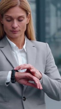 Ciddi derecede dakik Kafkasyalı yetişkin bir iş kadını kol saatini işaret ederek kameraman iş kadınına bakıyor şehir merkezindeki kadın işverenin saat başı portresini kontrol ediyor.