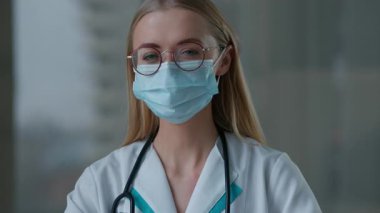 Üniformalı beyaz doktor kadın doktor maskesini gösteren portre, tamam işareti onaylıyor. Kamera içine bakıyor. Hemşire kadın terapist.