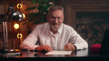 Kafkasyalı yazar elinde dolmakalem kâğıdı metin yazarı yazar kameraya bakıp gülümseyen, olgun, yaşlı, emekli iş adamı ev işleri bürosu belgelerine mektup yazıyor.