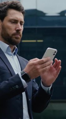 Şehirde başarılı bir Kafkas işadamı cep telefonuyla gülümseyen orta yaşlı iş adamı erkek işveren bina dışında akıllı telefon online internet mesajı kullanıyor.
