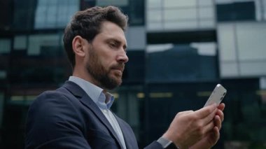 Kafkasyalı iş adamı cep telefonuyla akıllı telefonları tarıyor şehir dışında erkek iş adamı girişimci emlakçı cep telefonu cihaz bağımlısı cep telefonu uygulaması internete mesaj yüklüyor