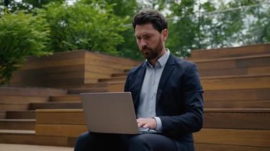 Üzüntülü Kafkasyalı iş adamı şehir dışında dizüstü bilgisayarda çalışıyor. İş adamı, işveren, iş adamı, internet, endişeli, stresli, işçi, hata, bilgisayar, e-posta sorunu.