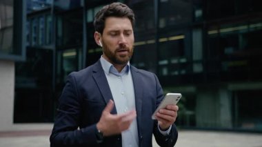 Kablosuz kulaklıklı beyaz bir işadamı cep telefonuna cevap veriyor. Yetişkin girişimci, erkek iş adamı, işveren, cep telefonu bilge işvereni. Cihaz yöneticisi şehir merkezini kullanarak konuşuyor.