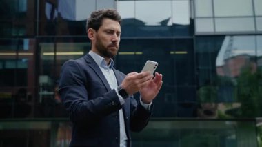 Şehirde başarılı bir Kafkas işadamı cep telefonuyla gülümseyen orta yaşlı iş adamı erkek işveren bina dışında akıllı telefon online internet mesajı kullanıyor.