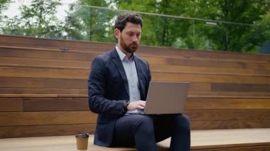 Beyaz iş adamı kameraya bakıp gülümsüyor. Şehirdeki bir adamın bilgisayarında çalışıyor. Orta yaşlı girişimci işveren. Serbest çalışan.