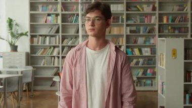 Kütüphanede gülümseyen beyaz bir erkek öğrenci. El hareketi yapıyor. Kitapçıda liseli gençleri tavsiye ediyor.