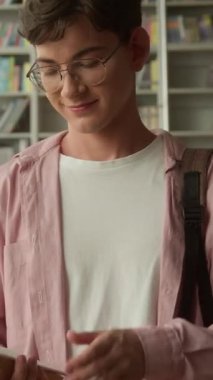 Kütüphanede kameraya bakıp gülümseyen beyaz erkek öğrenci edebiyat sınavları alan mutlu adam kitapçıda okumaya hazırlanıyor.