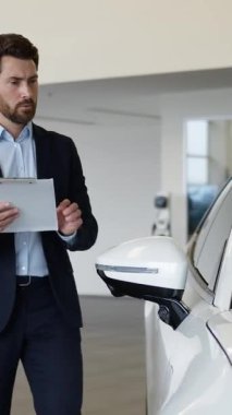 Kafkasyalı iş adamı elinde dosya tutuyor, belgeleri inceliyor, kapalı araba galerisi, galeri erkek işadamı yeni bir gözden geçirme yazısı yazıyor, araç kiralama, araç kiralama, araç kiralama, nakil kontrolü.