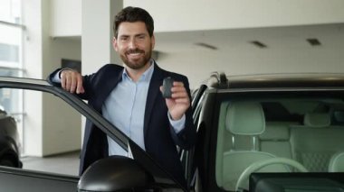 Neşeli Kafkasyalı iş adamı otomobil anahtarlarını kapalı galeride gösteriyor. Yeni araba alıcısı gülümseyen işadamı. Kameraya bakan güler yüzlü satıcı.