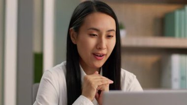 Pozitif Asyalı Japon işkadını ofis çalışanı bilgisayardan konuşuyor dizüstü bilgisayarcı kız işveren müdürü neşeli Koreli kadın iş kadını internet üzerinden iş görüşmesi yapıyor kapalı alanda iş görüşmesi yapıyor.