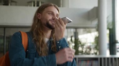 Mutlu gülümseyen beyaz erkek öğrenci sesli mesaj kaydediyor cep telefonlu adam akıllı telefon uygulamasına dikte ediyor üniversite akademisinde neşeli bir gülümseme.