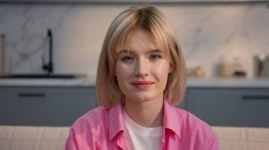 Kapalı kapılar ardında gülümseyen beyaz, genç bir kadın. Evdeki kanepede dinleniyor. Evde dinlenen genç bir kız öğrenciye bakıyor.