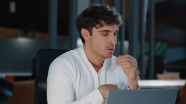 Yoğunlaşmış yorgun Kafkasyalı iş adamı gece şirketinde dizüstü bilgisayar kullanarak esniyor Avrupalı iş adamı bilgisayarını esnetiyor bilgisayar teknolojisi siber uzay son teslim tarihi aşırı uykulu erkek.