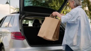 Açılmış otomobil bagajına paketler koyan Kafkasyalı yaşlı bir kadın. Emekli kadın. Alışveriş ekosistemi çantalarını araba kiralama, araba kiralama, araba kiralama, indirim teslimatı.