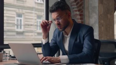 Hintli stresli iş adamı göz sorunu tahriş olmuş Arap iş adamı yorgun adam ofis bilgisayarında çalışan erkek bilgisayar uzmanı burun köprüsü baş ağrısı tutan gözlükler.