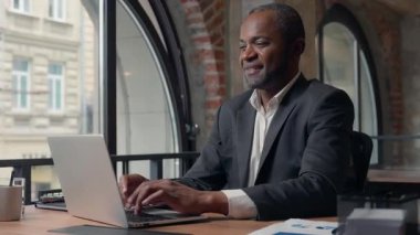 Afro-Amerikalı gülümseyen iş adamı, ofiste çalışan dizüstü bilgisayar işadamı, gülen orta yaşlı işçiler, bilgisayar teknolojisi işlerinde müşteriyle sohbet ederken mutlu mesut gülüyor.